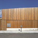 Front view of a modern wooden building with tall vertical slats and a wooden fence against a blue sky.