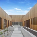 Symmetrical wooden courtyard with vertical panels and angled roof lines meeting at the center against a blue sky.