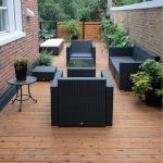 Wood deck patio with black wicker furniture and glass-topped coffee table, surrounded by potted plants and brick walls.