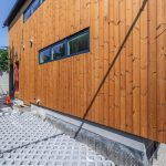 Wooden exterior wall with orange vertical planks, two long windows, and a textured concrete block walkway surface (construction site).